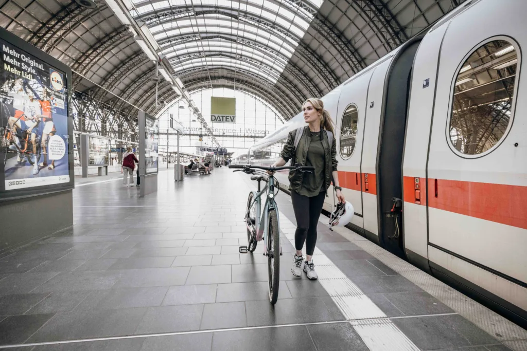 Frau auf dem Bahnsteig schiebt ihr Fahrrad am Zug entlang