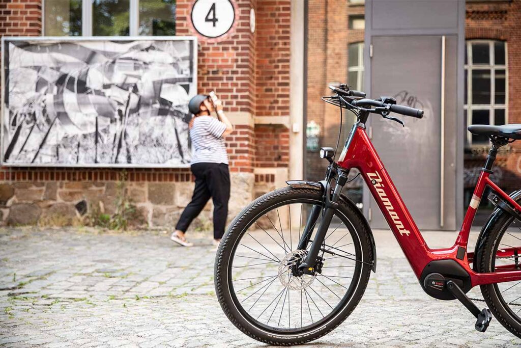 Rotes E-Bike vor Gebäude mit Frau im Hintergrund.