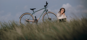 Frau mit Kopfhörern sitzt im Gras, daneben steht ein Fahrrad (Diamant 139)